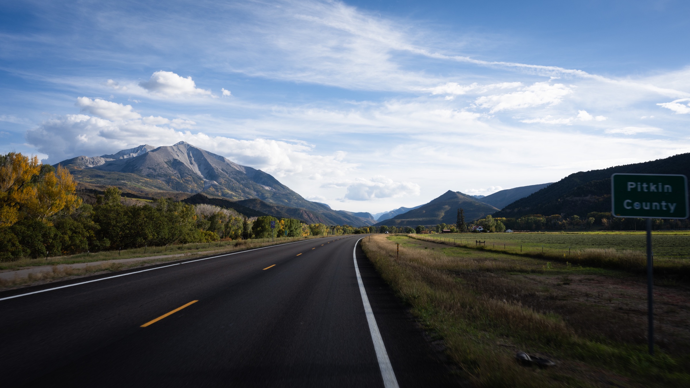 A mountain highway winding toward the Colorado Rockies under a wide sky